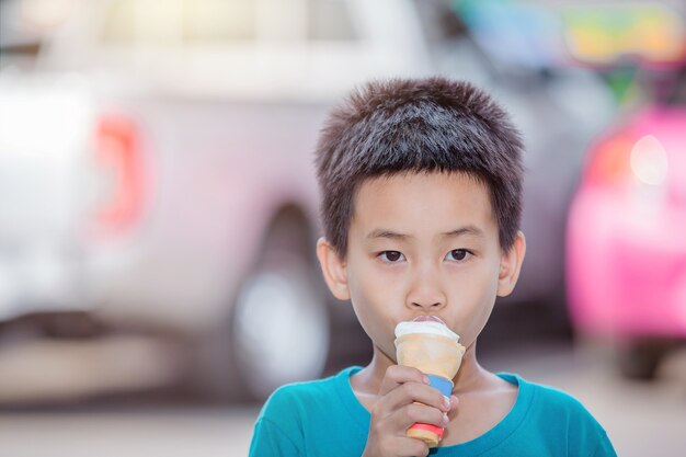 O menino está comendo sorvete em um estacionamento ao ar livre.