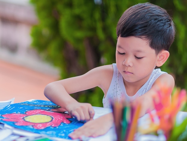 O menino está pintando a imagem colorida em casa.