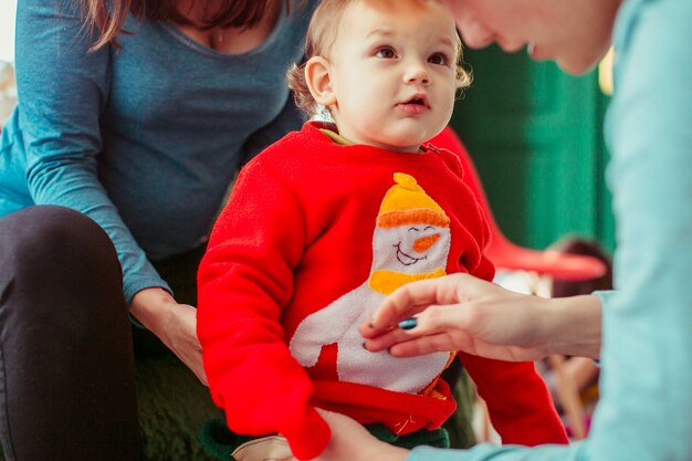 O menino pequeno está de pé e está olhando para a mãe no quarto