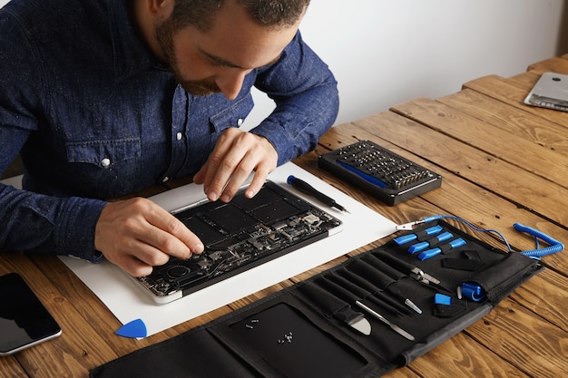 O mestre usa uma pinça esd em ângulo para remover a poeira das placas eletrônicas do laptop fino quebrado para consertá-lo e fazê-lo funcionar novamente