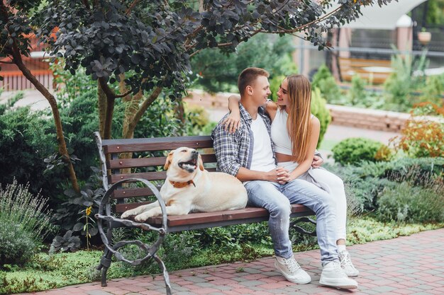 O momento de descanso! Lindo casal sorridente com seu cachorro no parque em um dia ensolarado