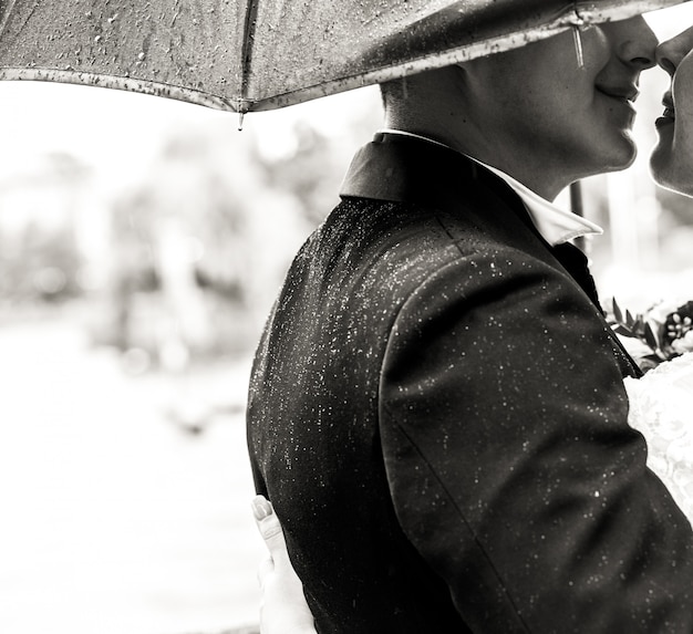 O noivo beija o pé macio da noiva sob o guarda-chuva na chuva