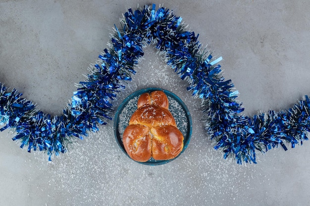 Foto grátis o ouropel azul em zigue-zague ao lado de um pão doce na mesa de mármore.