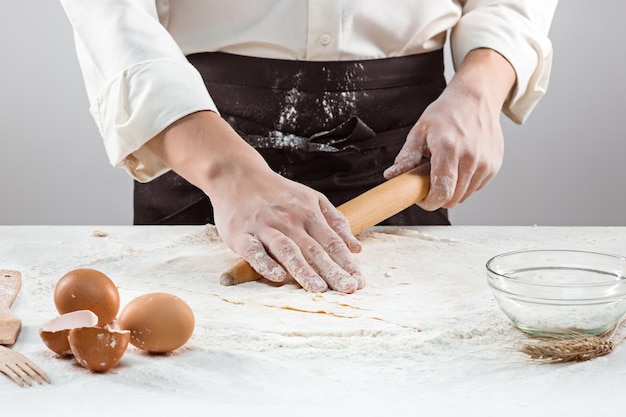 O padeiro fazendo pão, mãos masculinas, amassando uma massa, casaco de cozinha