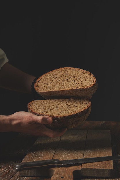 O padeiro tem nas mãos metades de pão de centeio no contexto da velha mesa marrom