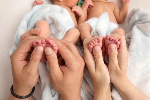 O pai e a mãe seguram as pernas dos gêmeos recém-nascidos. as mãos dos pais e os pés dos filhos. foto de alta qualidade Foto Premium