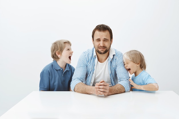 O pai não pode lidar com filhos enérgicos com mau comportamento. Pai sentado à mesa chorando de desespero enquanto meninos gritavam e discutiam