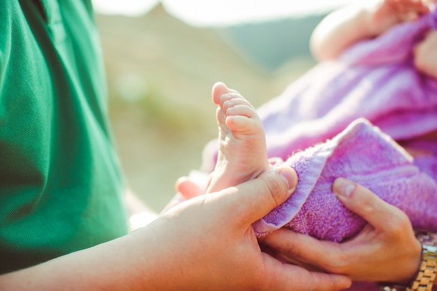 O pai segura os pés de seu filho envolvido em uma toalha violeta