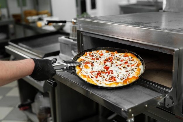 O pizzaiolo coloca pizza no forno para assar na cozinha do restaurante