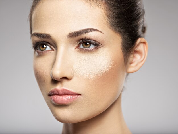 O pó de maquiagem cosmético seco está no rosto feminino. Conceito de tratamento de beleza. Garota faz maquiagem.