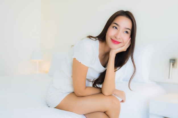 O retrato a mulher asiática nova bonita relaxa o sorriso feliz na cama com o cobertor branco do travesseiro