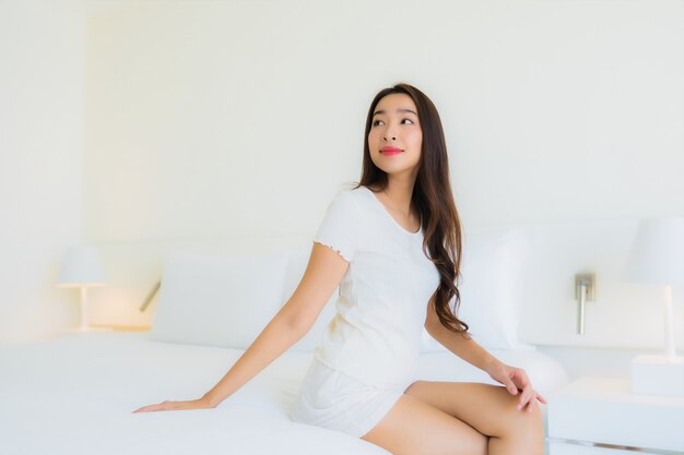 O retrato a mulher asiática nova bonita relaxa o sorriso feliz na cama com o cobertor branco do travesseiro