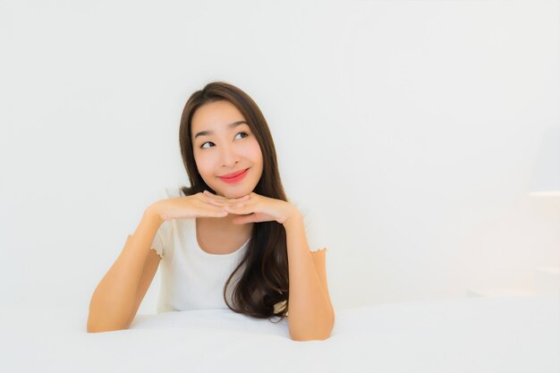 O retrato a mulher asiática nova bonita relaxa o sorriso feliz na cama com o cobertor branco do travesseiro