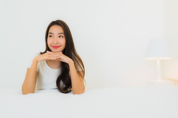 O retrato a mulher asiática nova bonita relaxa o sorriso feliz na cama com o cobertor branco do travesseiro