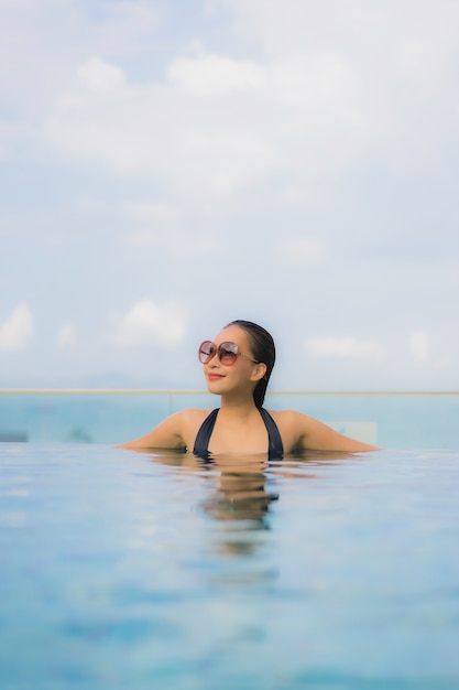 O retrato as mulheres asiáticas novas bonitas sorri feliz relaxa a piscina ao ar livre no recurso