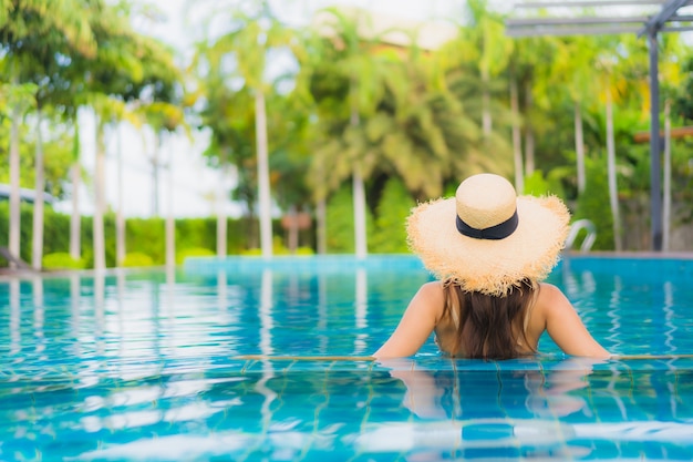 O retrato as mulheres asiáticas novas bonitas sorri feliz relaxa a piscina ao ar livre no recurso