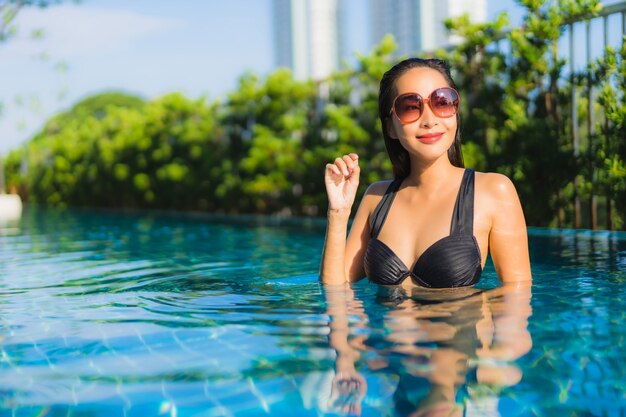 O retrato as mulheres asiáticas novas bonitas sorri feliz relaxa a piscina ao ar livre no recurso