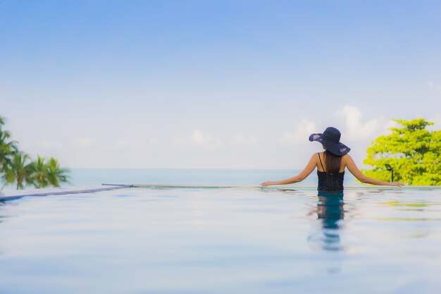 O retrato as mulheres asiáticas novas bonitas sorri feliz relaxa a piscina exterior no hotel