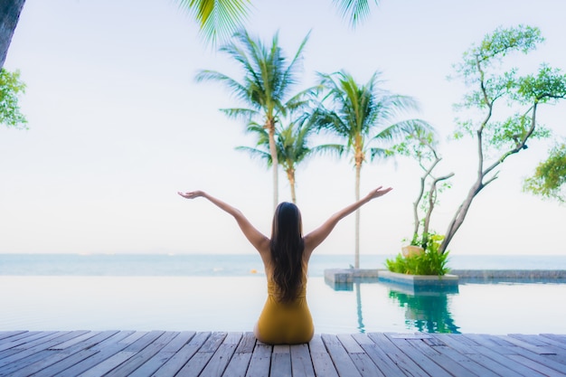 O retrato as mulheres asiáticas novas bonitas sorri feliz relaxa em torno da piscina exterior