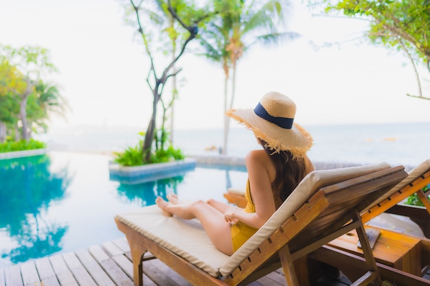 O retrato as mulheres asiáticas novas bonitas sorri feliz relaxa em torno da piscina exterior