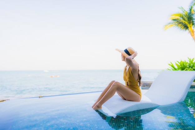 O retrato as mulheres asiáticas novas bonitas sorri feliz relaxa em torno da piscina exterior