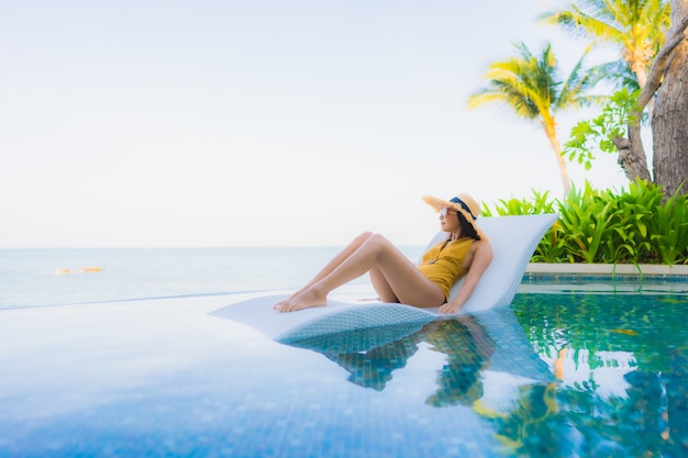 O retrato as mulheres asiáticas novas bonitas sorri feliz relaxa em torno da piscina exterior