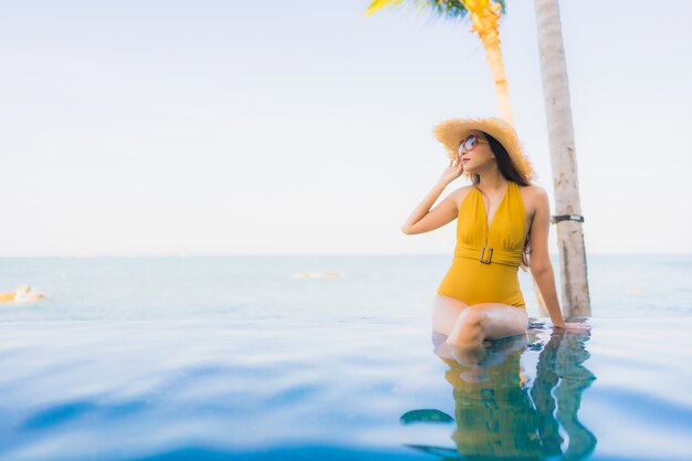 O retrato as mulheres asiáticas novas bonitas sorri feliz relaxa em torno da piscina exterior