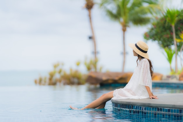 O retrato asiático novo bonito da mulher sorri feliz relaxa em torno da piscina no hotel resort