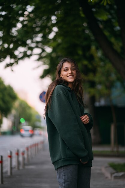 O retrato da menina bonito com cabelo longo olha a câmera na cidade na rua fundo.