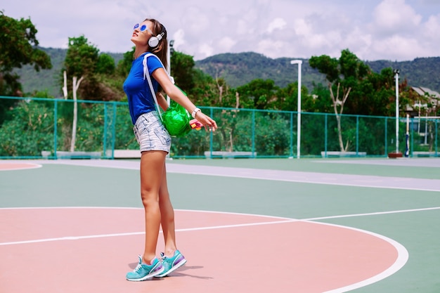 Foto grátis o retrato da moda de jovem apto mulher esportiva posando ao ar livre no verão tem um dia ensolarado, vestindo roupas esportivas de néon brilhante costas e óculos de sol.