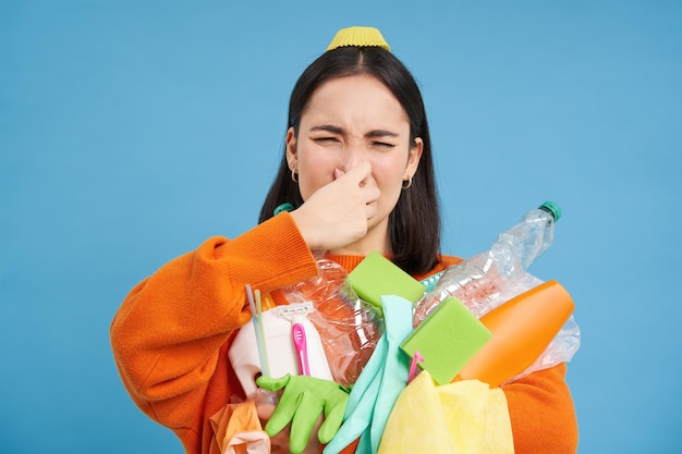 Foto grátis o retrato da mulher fecha o nariz de digust segurando itens plásticos sujos de lixo fedorento e bo vazio