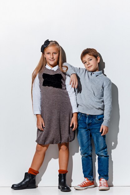 O retrato de um menino bonito e uma menina com roupas jeans elegantes, olhando para a câmera no estúdio