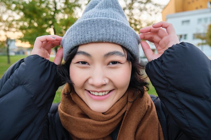Foto grátis o retrato de uma linda garota asiática de chapéu e cachecol anda pela cidade em um clima frio de primavera sorri e l