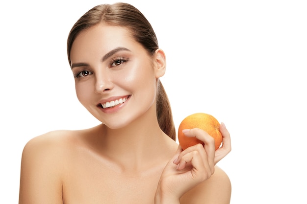 O retrato de uma mulher sorridente caucasiano atraente, isolado na parede branca com frutas laranja. A beleza, cuidado, pele, tratamento, saúde, spa, cosmético