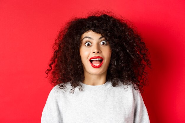 O retrato do close up da mulher excitada com o cabelo encaracolado gritou surpreso e espantado ao verificar o d ...