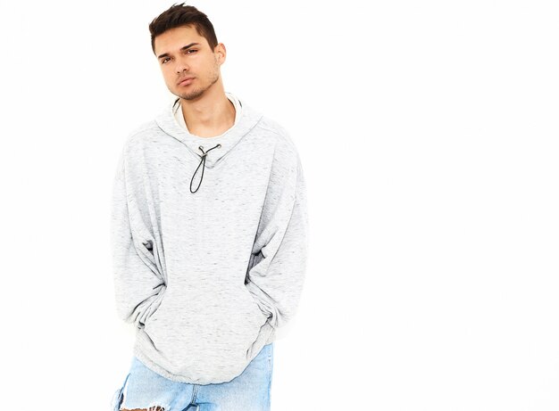 O retrato do homem modelo considerável novo vestiu-se na roupa ocasional cinzenta do hoodie que levanta na parede branca. Isolado