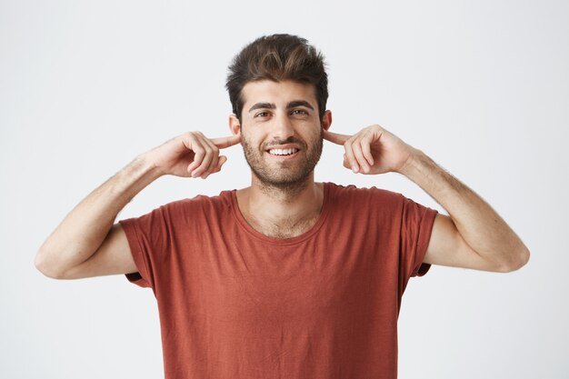 O retrato do jovem macho caucasiano irritado com os olhos fechados, tapando os ouvidos com os dedos, não suporta barulho alto ou ignora situações ou conflitos desagradáveis estressantes. Emoções humanas negativas