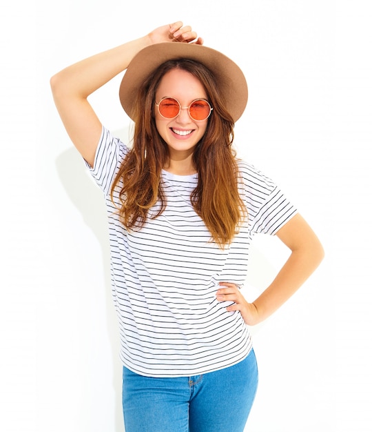 O retrato do modelo de mulher de riso à moda novo no verão ocasional veste-se no chapéu marrom com a composição natural isolada na parede branca. Piscando