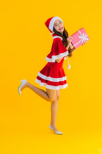 O retrato e o chapéu e as roupas asiáticos novos bonitos do Natal sorriem felizes com caixa de presente vermelha