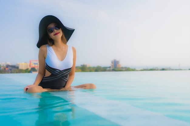 O retrato feliz asiático novo bonito da mulher relaxa em torno da piscina exterior no recurso do hotel