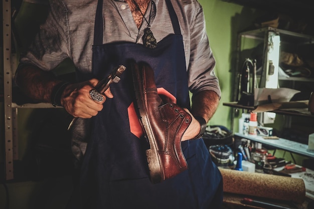 O sapateiro diligente está trabalhando na sola do sapato usando uma ferramenta especial em seu local de trabalho escuro.