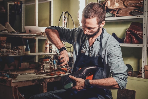 O sapateiro talentoso está trabalhando em um par de sapatos masculinos negros em sua oficina.