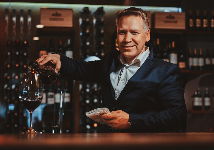 Foto grátis o sommelier de vinho elegante e arrumado está servindo vinho tinto no copo para prová-lo.