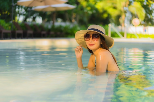 O sorriso feliz das jovens mulheres asiáticas bonitas relaxa em torno da piscina exterior no recurso do hotel para viajar nas férias