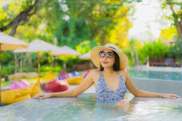 O sorriso feliz das jovens mulheres asiáticas bonitas relaxa em torno da piscina exterior no recurso do hotel para viajar nas férias