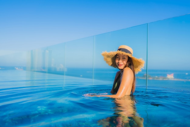 O sorriso feliz das jovens mulheres asiáticas bonitas relaxa em torno da piscina exterior no recurso do hotel para viajar nas férias