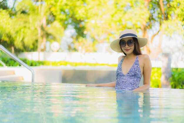 O sorriso feliz das mulheres asiáticas novas bonitas relaxa em torno da piscina exterior no recurso do hotel