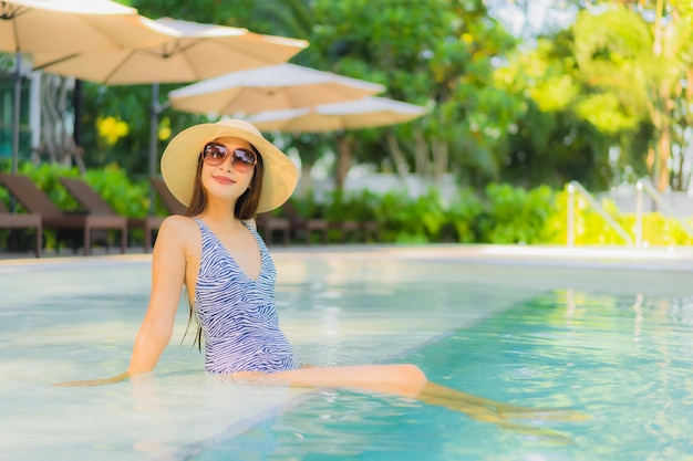 O sorriso feliz das mulheres asiáticas novas bonitas relaxa em torno da piscina exterior no recurso do hotel