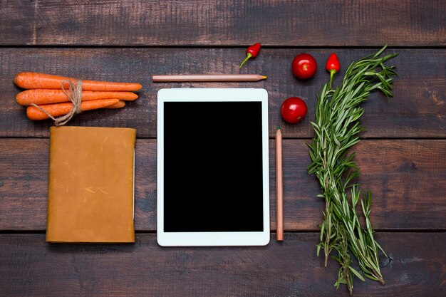 O tablet, notebook, pimentão fresco e amargo no fundo da mesa de madeira