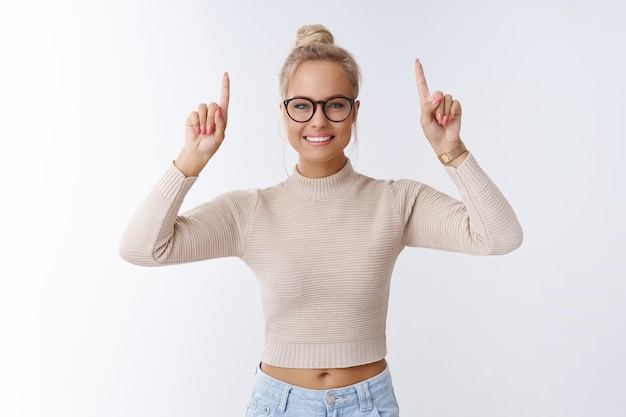 O tempo avança. retrato de glamour atraente e mulher loira elegante com óculos da moda apontando para cima e sorrindo alegremente, dando bons conselhos, indicando uma promoção perfeita sobre fundo branco